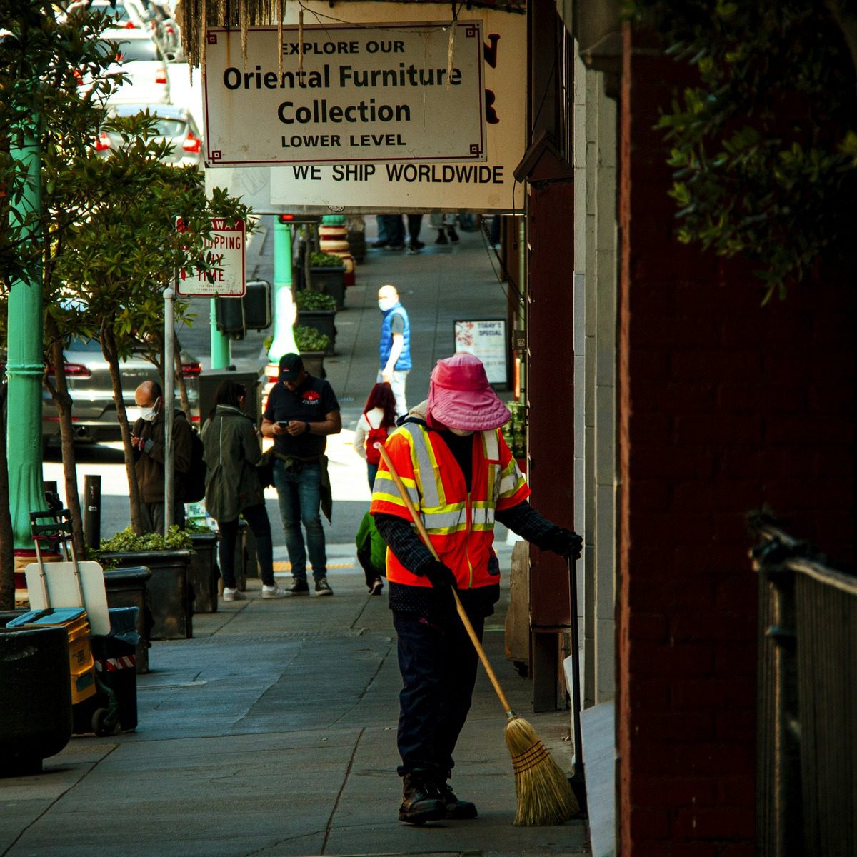 Municipal maintenance worker sweeping debris from a busy commercial sidewalk, representing municipal street sweeper services near me.