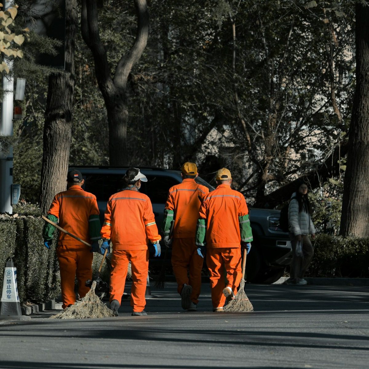 Municipal maintenance crew in high-visibility uniforms sweeping debris from a tree-lined roadway, representing municipal street sweeper services in Santa Clarita, CA.
