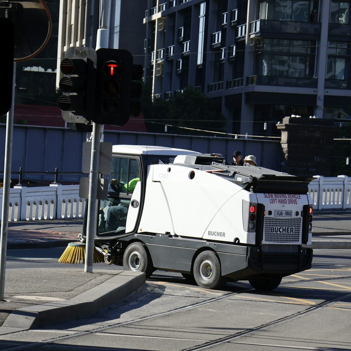 Municipal street sweeper truck using rotating curb brushes to clean debris from an urban roadway, representing municipal street sweeper services near me.