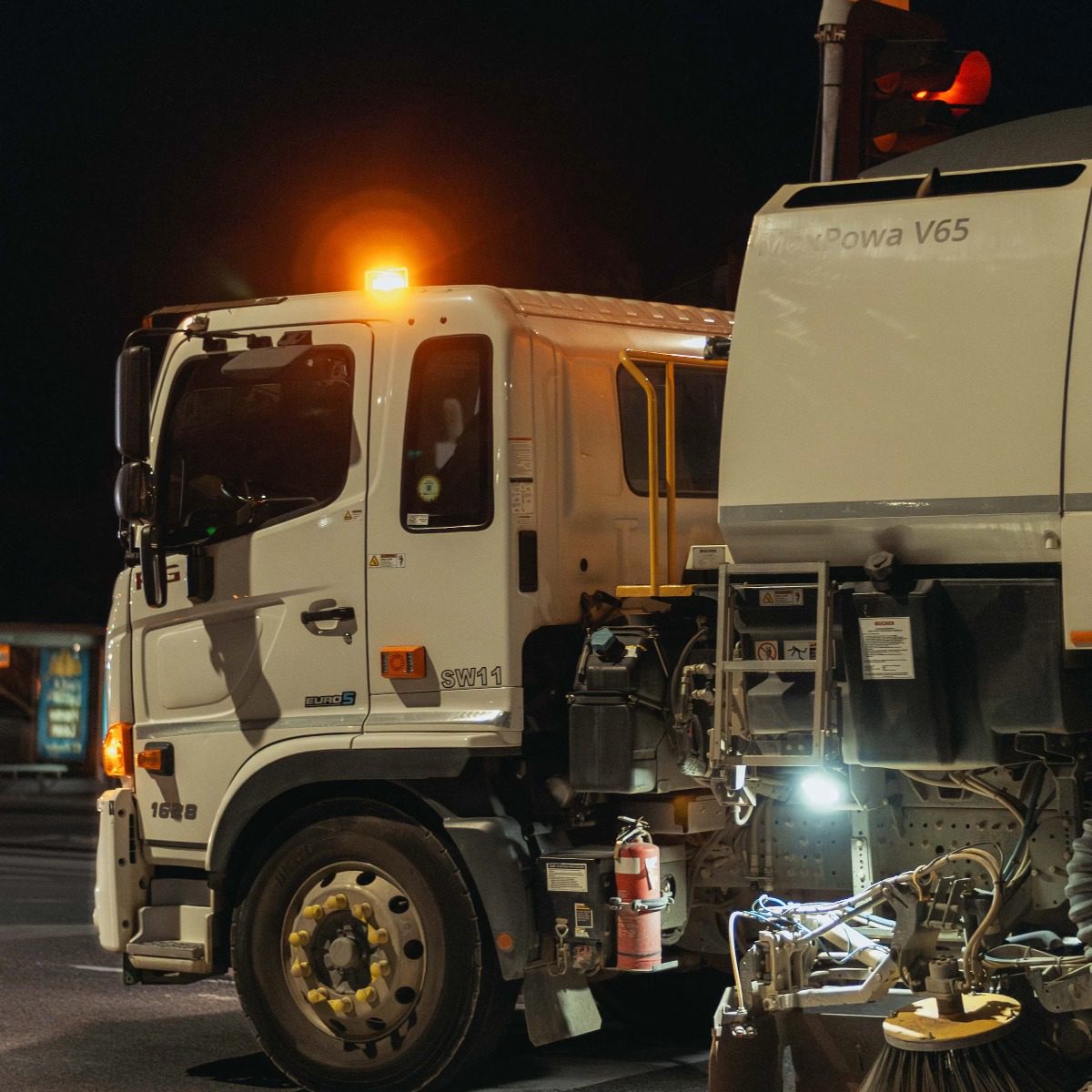 Municipal street sweeper truck operating at night with illuminated sweeping equipment and curb brushes, representing municipal street sweeper services in Woodland Hills, CA.